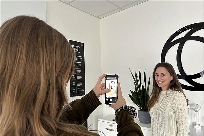 A woman is taking a professional photograph of her colleague in an office.